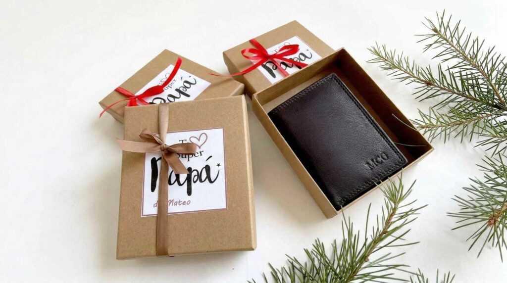 Caja de regalo artesanal abierta que muestra una cartera de cuero marrón oscuro con iniciales grabadas.