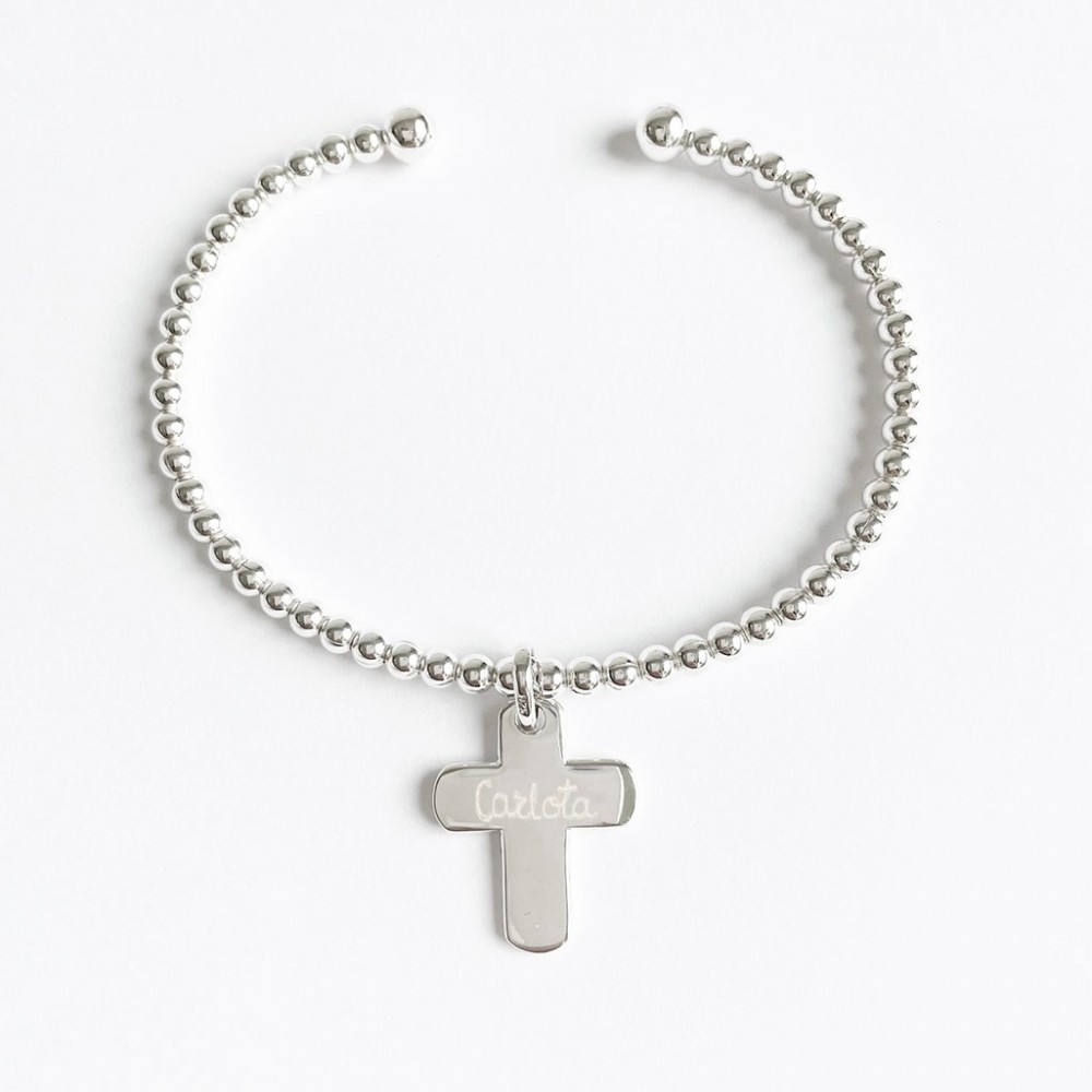 Pulsera rígida de bolitas de plata de ley con dije de cruz colgado, grabada con el nombre en letra cursiva sobre fondo blanco.