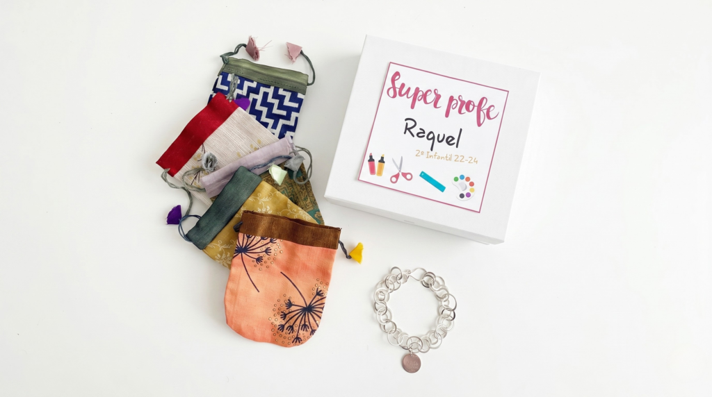 Kit de regalo para profesores que incluye una caja personalizada con la etiqueta 'Super profe', bolsas de tela con cordón de diferentes colores y una pulsera de plata con cadena personalizada.